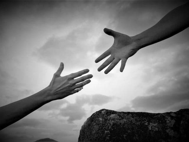 Two hands reaching toward each other against a cloudy sky