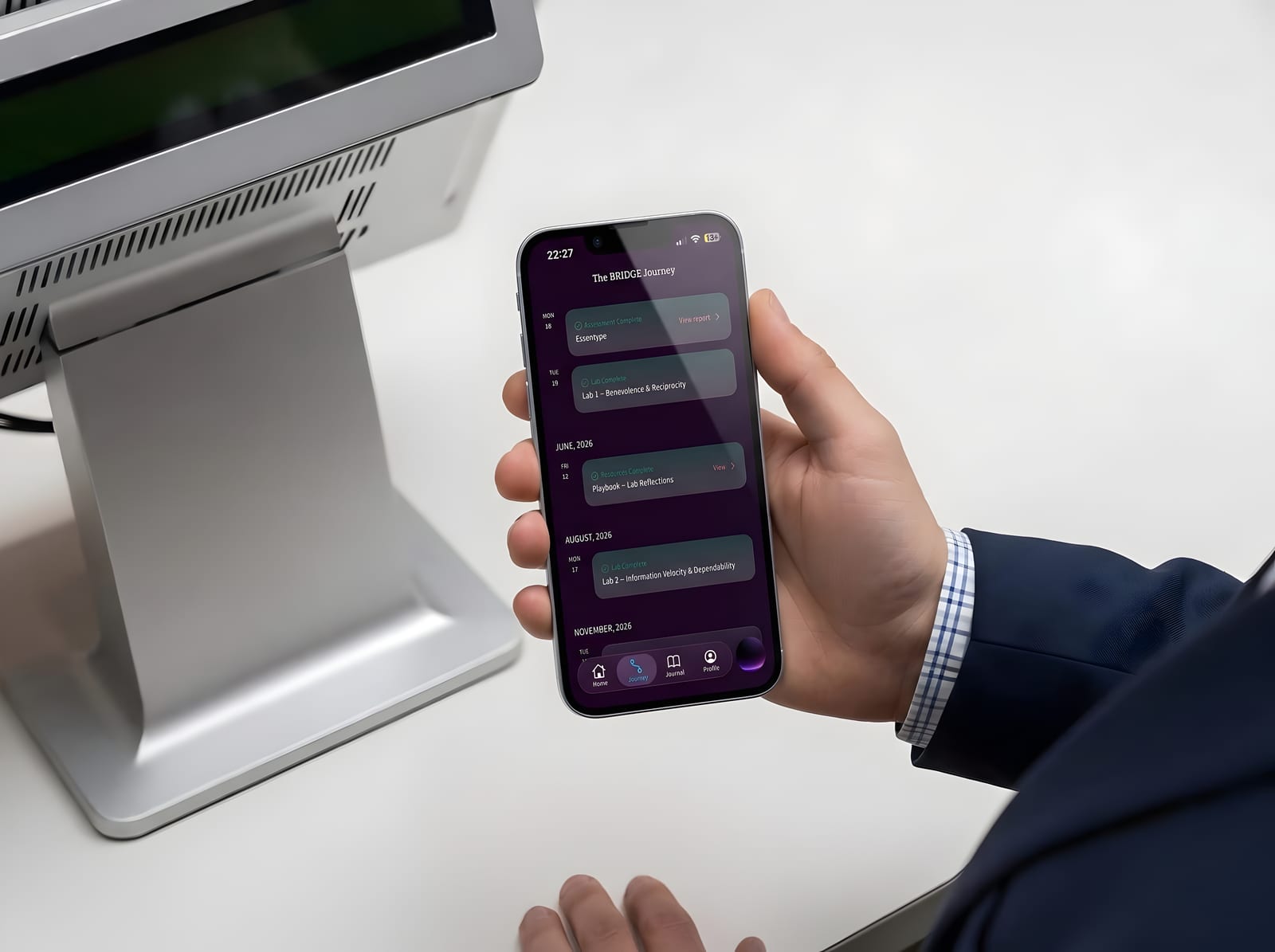 A hand holding a phone showing the Invincible YOU app’s BRIDGE Journey — a timeline of labs and reflections